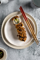 A crispy sushi roll on a white plate with chopsticks on neutral background - PhotoDune Item for Sale