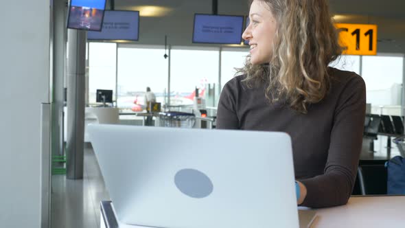 Smiling Girl Works on Laptop Sitting in Airport Lounge Cafe