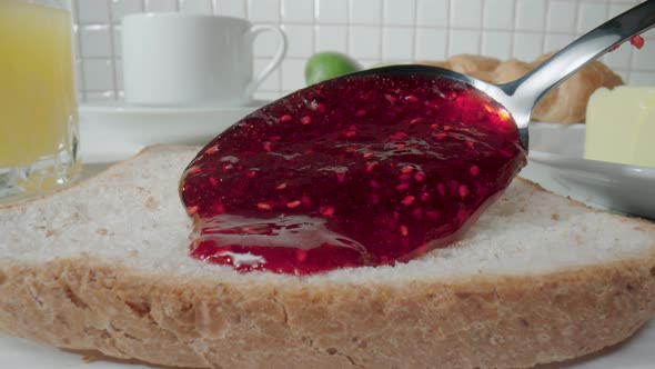 A Spoon Pouring Raspberry Jam Onto a Piece of Bread Toast