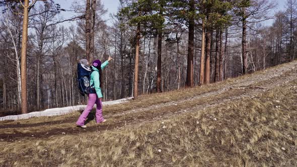 A Young Active Mother Walks Through the Spring Forest Carrying Her Young Son in a Backpack