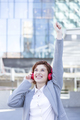 Happy young woman in suit listening to music with headphones in city. - PhotoDune Item for Sale