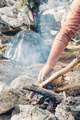 Man hiker putting firewood into flame while making bonfire near tent in mountain - PhotoDune Item for Sale