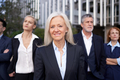 Business woman standing outdoors and looking at camera with her colleagues in the background - PhotoDune Item for Sale