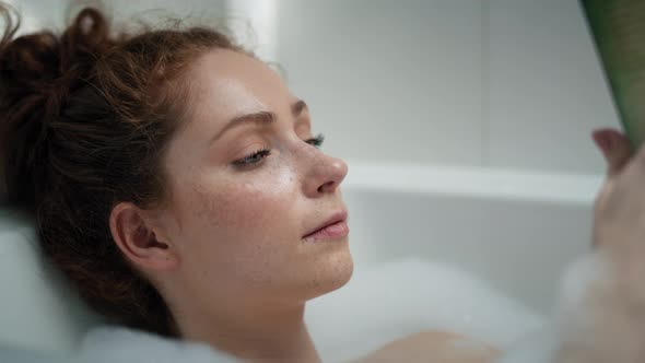 Caucasian redhead woman taking a bath and reading a book. Shot with RED helium camera in 4K.