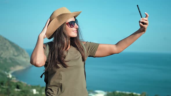 Portrait of Smiling Woman Traveler in Hat and Sunglasses Posing and Taking Selfie Using Smartphone