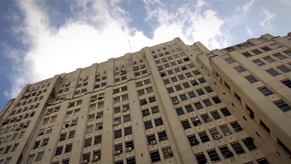 Looking Up at a Tall Old Building with Blue Sky and Clouds Above.