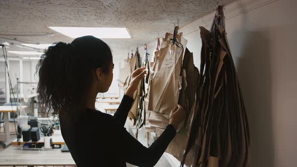 Young Multiethnic Woman Fashion Designer of Sewing Workshop is Choosing a Pattern or Mold Hanging on