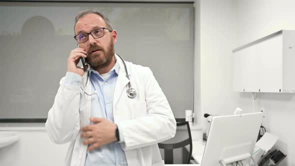 Doctor is Talking on the Cell Phone By the Window at a Modern Bright Office Background