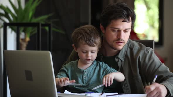 Father is trying to work and play with a little boy at same time at home.