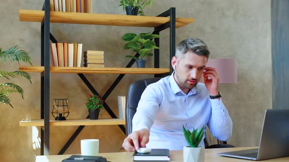 Bearded businessman in home office puts on wireless earphones starts using laptop computer