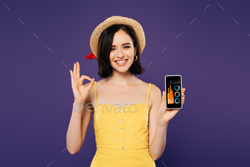 smiling pretty girl in straw hat holding smartphone with business analytics app and showing ok sign