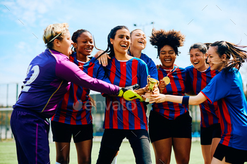 Excited female soccer players with a winning trophy celebrating on playing field.