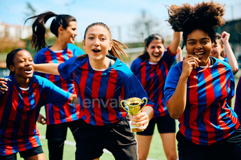 Cheerful female soccer players celebrating winning a trophy on a championship.