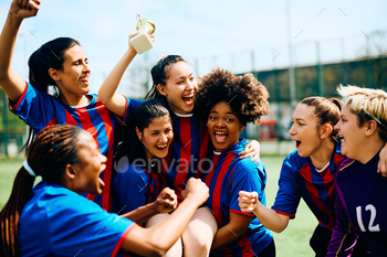 Excited female soccer players having fun while celebrating winning the tournament trophy.