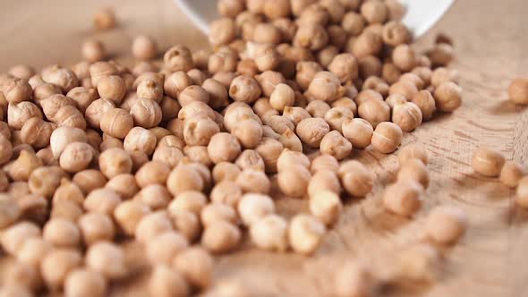 Chickpea beans are poured onto a wooden board from a white bowl in slow motion