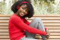 Smiling young afro woman on park bench listening to music and looking at camera. - PhotoDune Item for Sale