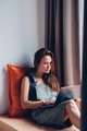 College woman student uses a laptop computer while sitting on a windowsill. - PhotoDune Item for Sale