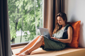 Young woman uses a laptop computer while sitting on a windowsill in hotel - PhotoDune Item for Sale