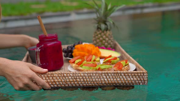 A Young Woman Tourist Has Her Own Personal Breakfast on a Floating Table in a Private Swimming Pool