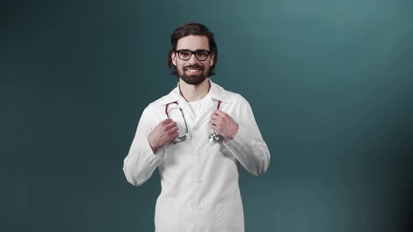 Portrait of Confident Young Medical Doctor in Glasses and with Statoskope on Green Background