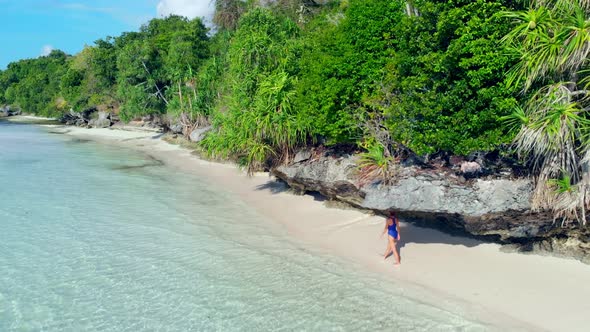 Aerial: woman walking on desert beach, tropical island white sand beach turquoise caribbean sea