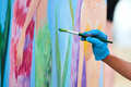 Artist's hand in blue gloves with paintbrush painting colorful picture at outdoor art festival - PhotoDune Item for Sale