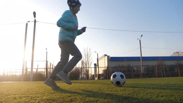 A Child Girl Playing with Soccer Ball Under Sun Light. Green Field in City Park at Sunny Day. Action