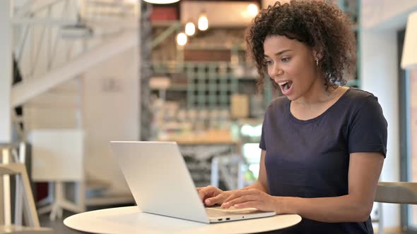 Young African Woman Celebrating Success on Laptop in Cafe 