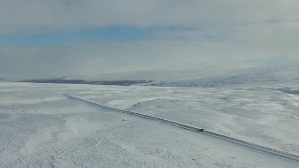 4K drone footage of car driving in snowy landscape in Iceland.