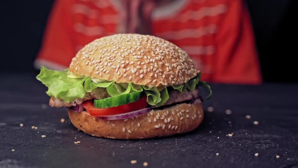 teenager hands take a tasty hamburger lying on the table close up. Delicious grilled burger