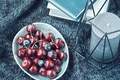 Bowl full of ripe red cherries candlestick and books on a dark blue knitted blanket.  - PhotoDune Item for Sale
