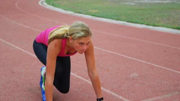 Front view of Caucasian female athlete taking starting position and running on a track at sports ven