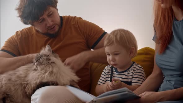 Family Sitting on Yellow Couch with Their Fluffy Cat Pet and the Baby Holding Pencils