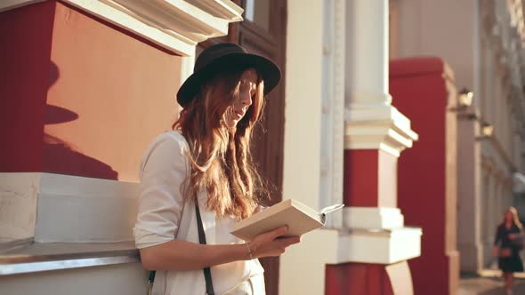 Young Beautiful Girl in Hat Reading Book in City Park