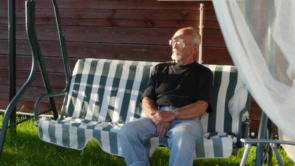 Elderly Man Sitting on Swing Near the Country House