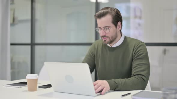 Young Businessman Celebrating Success While Using Laptop in Office