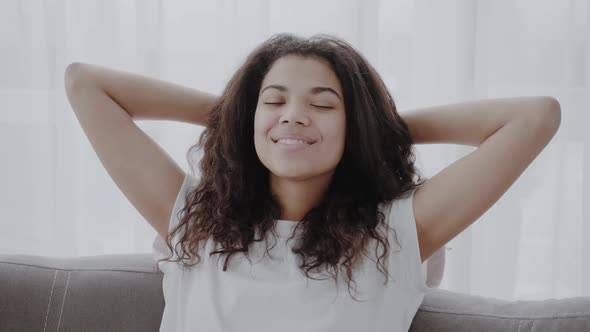 Happy African American Young Woman Sit Relax on Cozy Couch Hands Over Head Happy to Move to New