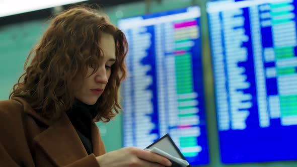 A Woman in Business Clothes Takes Out Her Passport and Printed Plane Ticket Looks Schedule on