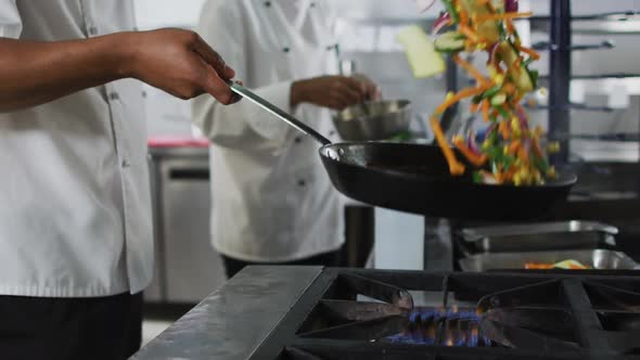 Midsection of mixed race male chef frying vegetables in pan