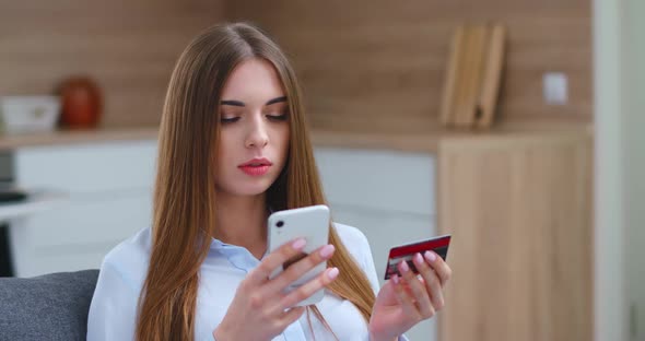 Young Woman Is Sitting on the Sofa in the Living Room and Pays for Purchases Online Using a