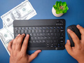 Top view someone hand typing wireless keyboard and holding mouse with banknotes on blue background. - PhotoDune Item for Sale