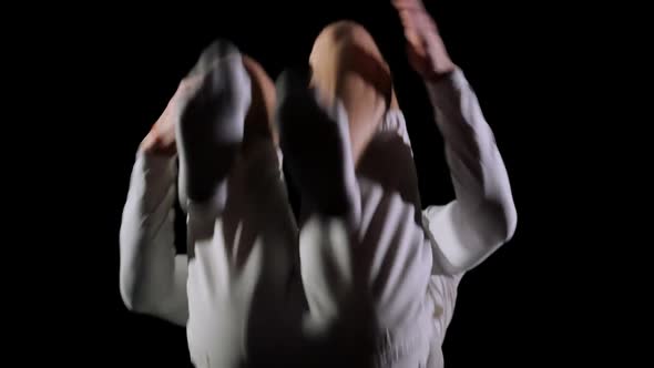 Young Handsome Male Acrobat Gymnast in White Clothes on a Black Background Makes Jumps and Shows