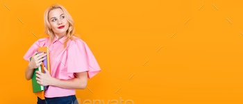  with red lips in pink shirt and jeans with pile of books isolated on orange background with copyspace. Horizontal picture.
