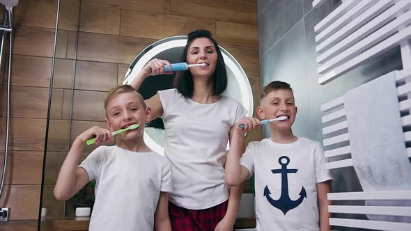 Mother and Her Two Sons which Cleaning Their Teeth with Toothbrushes in the Bathroom