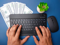 Top view someone hand typing wireless keyboard with banknotes on blue background. - PhotoDune Item for Sale
