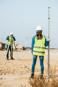 Selective focus of surveyors with survey ruler and digital level on construction site