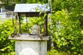 Old well with a rusty bucket in the yard. Watering. Bright fresh summer greenery view. Countryside.  - PhotoDune Item for Sale