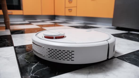 The Robot Vacuum Cleaner Cleans in the Modern House on the Tiles Floor at Kitchen