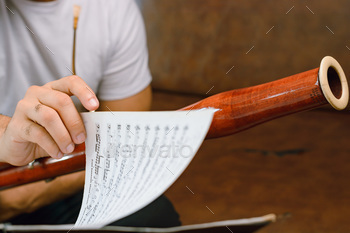 closeup of bassoonist male hand turning sheet music page on music stand, focus on hand.