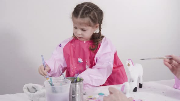 Little girl painting paper mache figurines with acrylic paint  for her homeschooling art project.